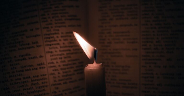 Close-up of candle flame illuminating an open book, creating a warm, introspective atmosphere.